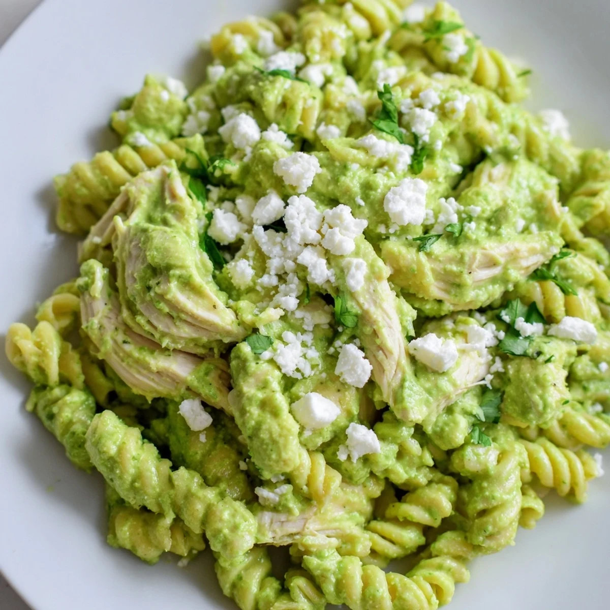 Close-up of creamy Cilantro Lime Chicken Pasta with shredded chicken and rotini coated in tangy yogurt sauce, garnished with fresh cilantro and lime wedges.  