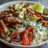 A close-up view of a Sheet Pan Fajita Bowl topped with fresh avocado slices, cilantro, and lime wedges.  