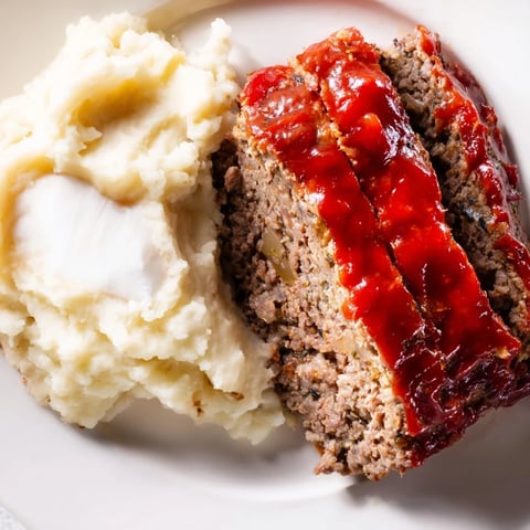 Juicy Classic Meatloaf & Mashed Potatoes, steaming hot, served alongside fluffy, creamy mashed potatoes.