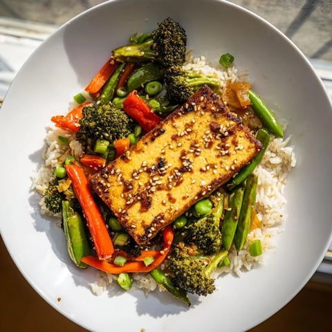 Golden-brown pressed tofu steaks glistening, served atop vibrant stir-fried vegetables and fluffy rice.
