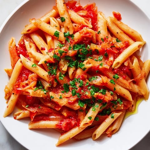 Steaming bowl of penne all'arrabbiata: vibrant red sauce coats perfectly cooked penne pasta.
