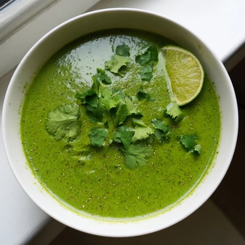 A bowl of creamy green Spinach Coriander Lemongrass Soup garnished with fresh herbs and lime wedges.