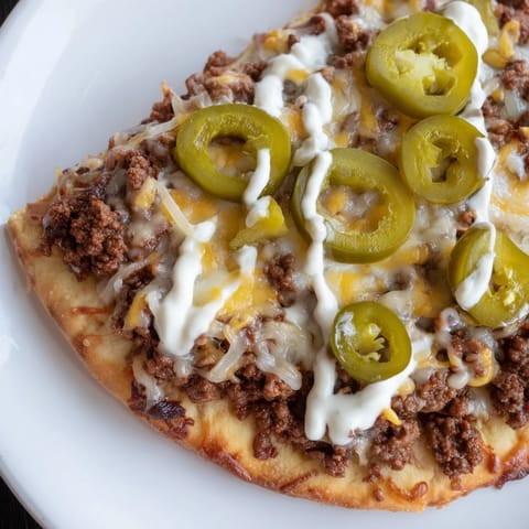 A close-up of a bubbling Ground Beef Taco Pizza, showcasing its flavorful meaty topping and crust.