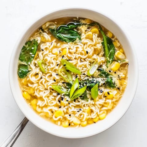 A steaming bowl of Elevated Ramen Egg Drop Soup garnished with fresh scallions and toasted sesame seeds.