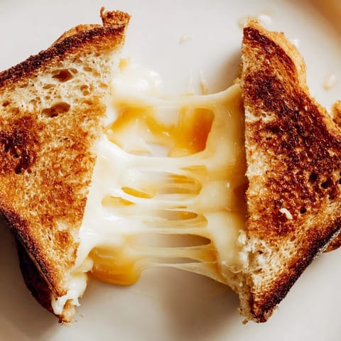 A plate featuring two warm Triple Cheese Sourdough Grilled Cheese sandwiches, perfect for dipping into a bowl of tomato soup.