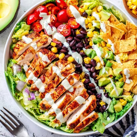 A generous bowl of Crunchy Taco Chicken Salad features creamy avocado, melted cheddar, and a drizzle of zesty lime dressing.
