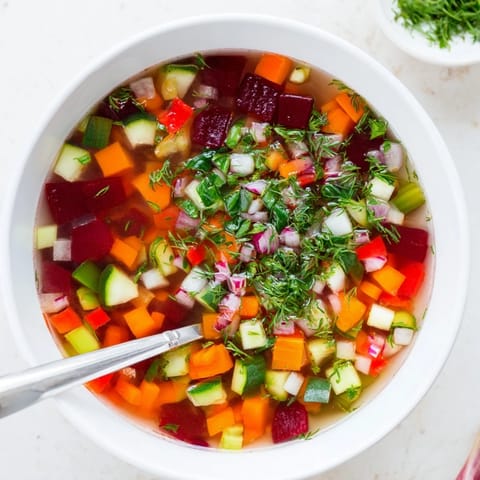 A steaming bowl of Rainbow Vegetable Detox Soup brims with colorful chopped beets, carrots, and fresh herbs.