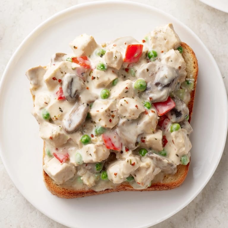 Warm chicken à la king over buttered toast, a hearty meal with cooked chicken and vegetables.