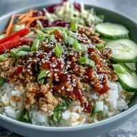 Steamed jasmine rice topped with spicy ground turkey, crunchy rainbow veggies, and a creamy bang bang sauce in a white bowl.  
